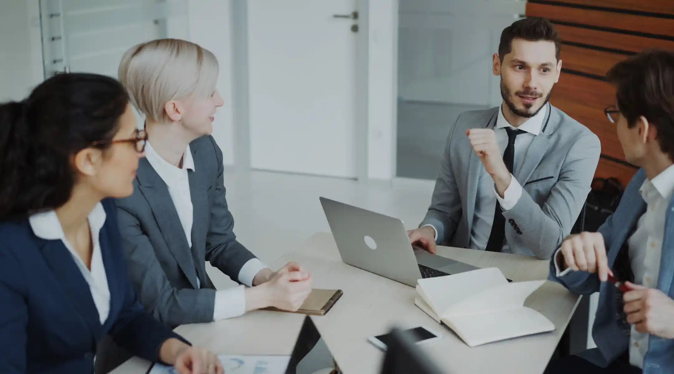 Man in boardroom with laptop chatting with colleagues Man in boardroom with laptop chatting with colleagues
