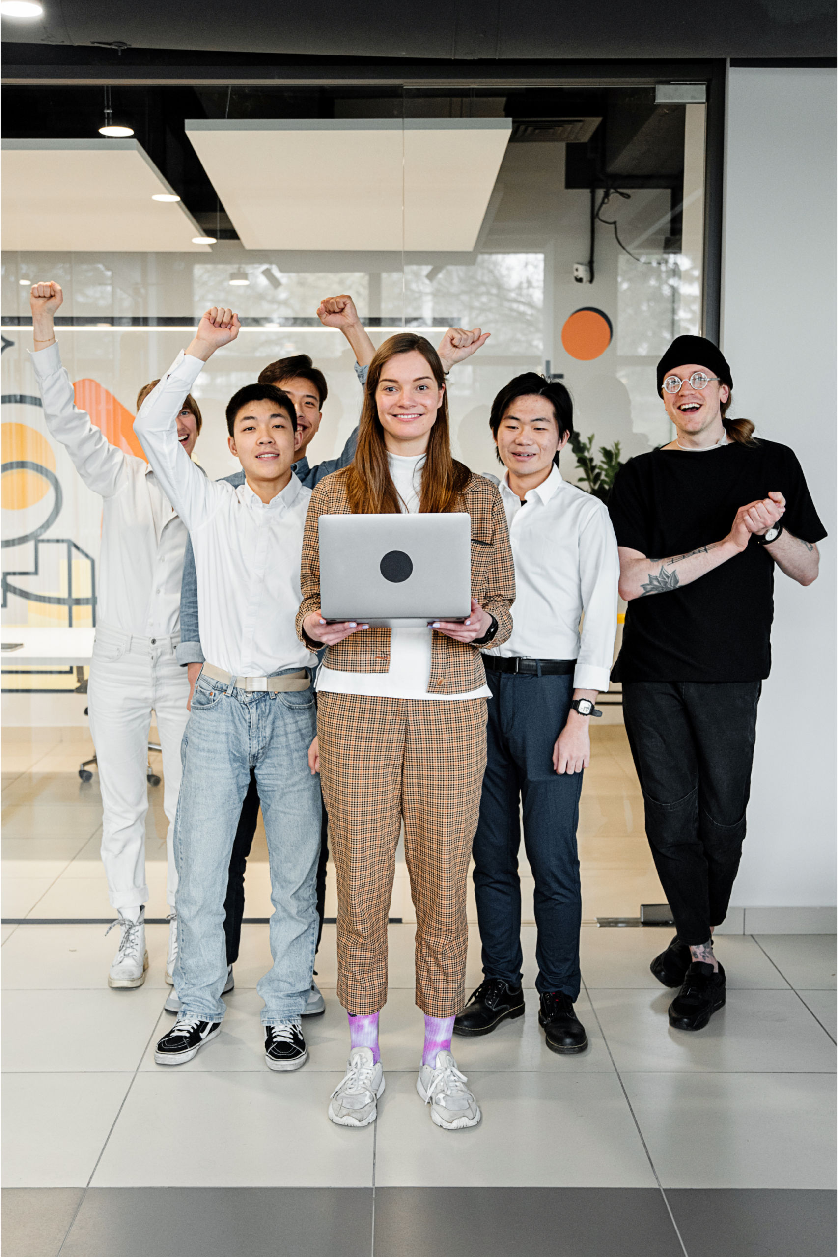 Smiling woman holding a laptop in front of five cheering colleagues, some with fists raised, in a modern office