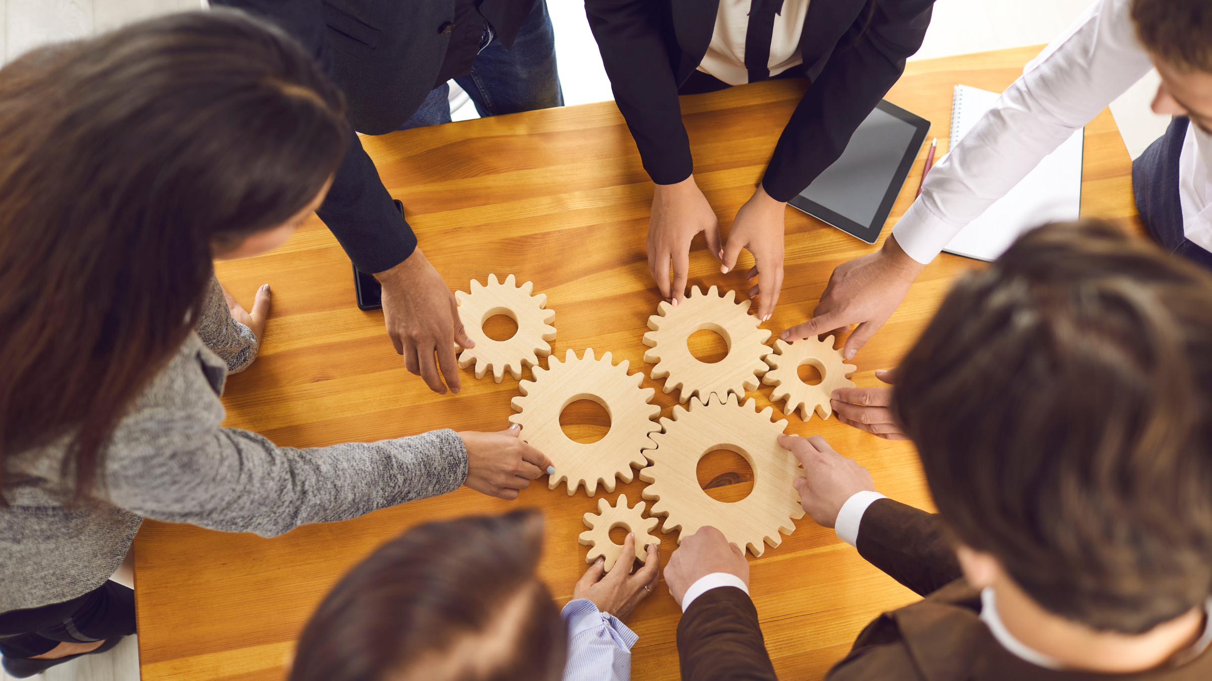 Team Working Together – Sincron HR Guided Implementation Overhead view of a team around a table, fitting wooden gears together